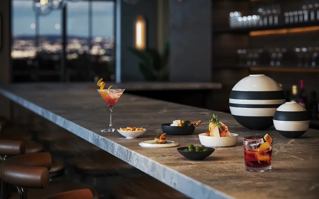 Villeroy & Boch: ZOA Studio rendering of an aperitivo setting on a bar counter at dusk, with La Petite Boule vessels and the city beyond